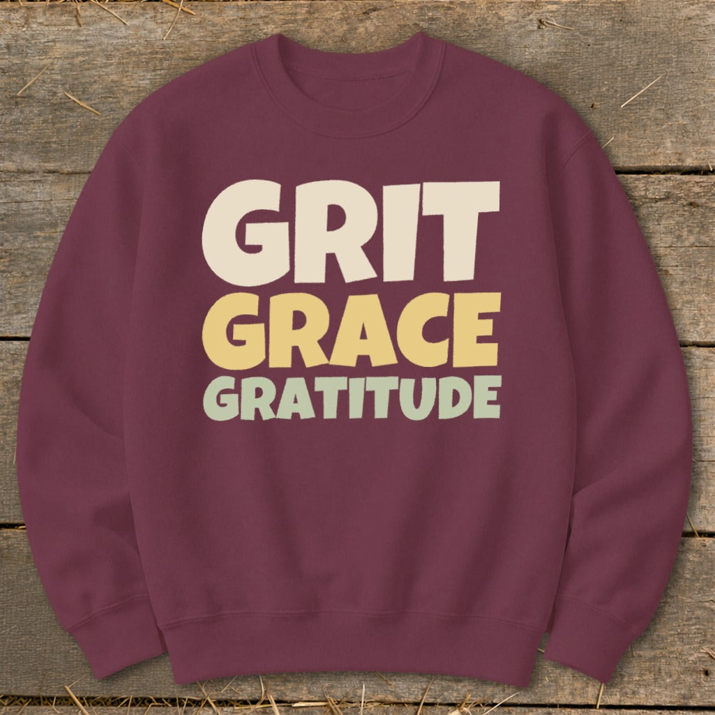 Maroon crewneck sweatshirt featuring the stacked text GRIT GRACE GRATITUDE in cream, yellow, and light green.