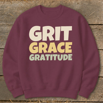 Maroon crewneck sweatshirt featuring the stacked text GRIT GRACE GRATITUDE in cream, yellow, and light green.