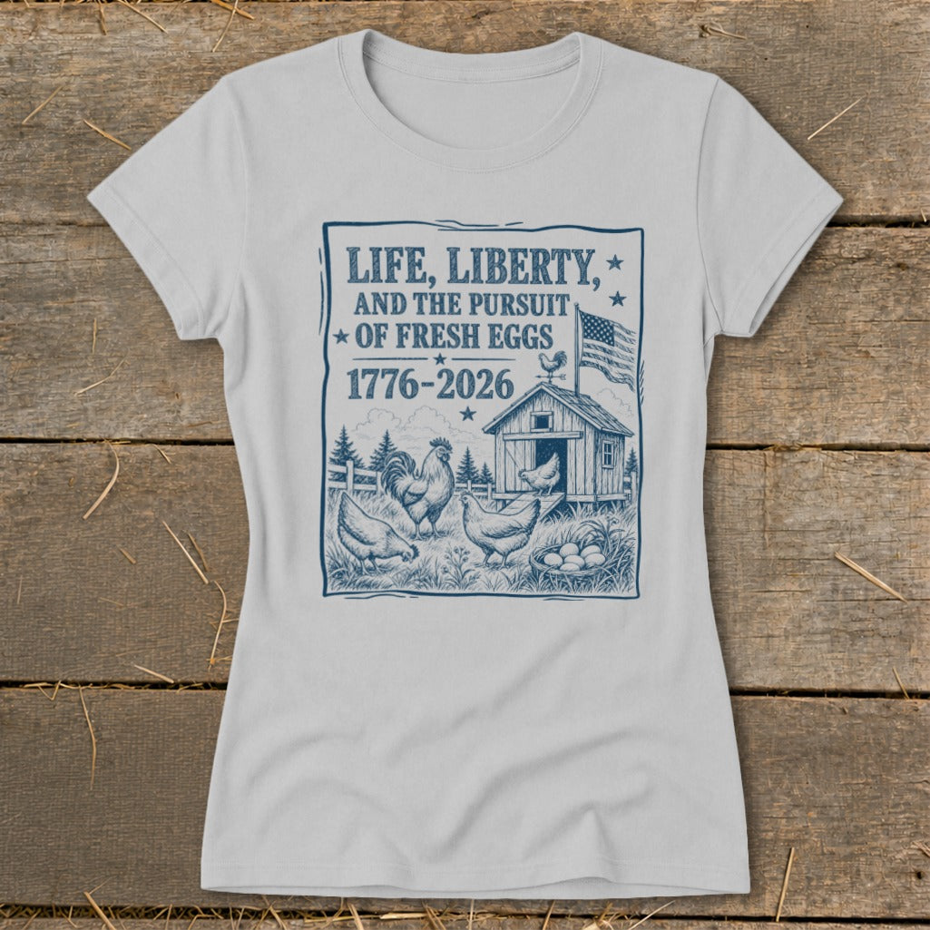 Light gray t-shirt with blue graphic: "Life, Liberty, And The Pursuit Of Fresh Eggs 1776-2026".