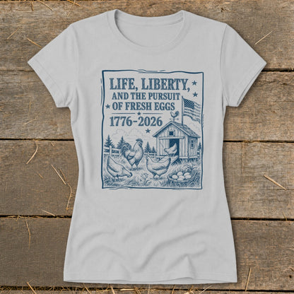 Light gray t-shirt with blue graphic: "Life, Liberty, And The Pursuit Of Fresh Eggs 1776-2026".