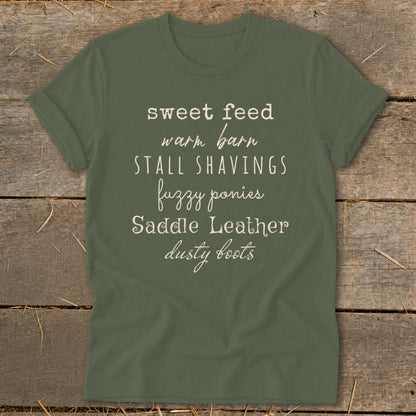 Green t-shirt with "sweet feed, warm barn, stall shavings, fuzzy ponies, saddle leather, dusty boots" text.