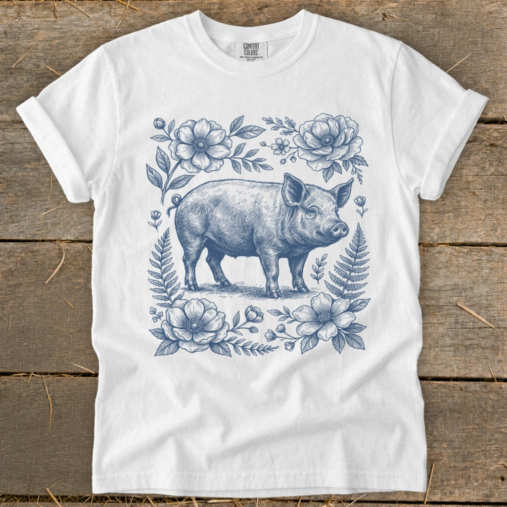 White t-shirt with a blue line drawing of a pig surrounded by flowers and ferns.
