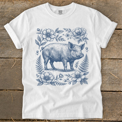 White t-shirt with a blue line drawing of a pig surrounded by flowers and ferns.