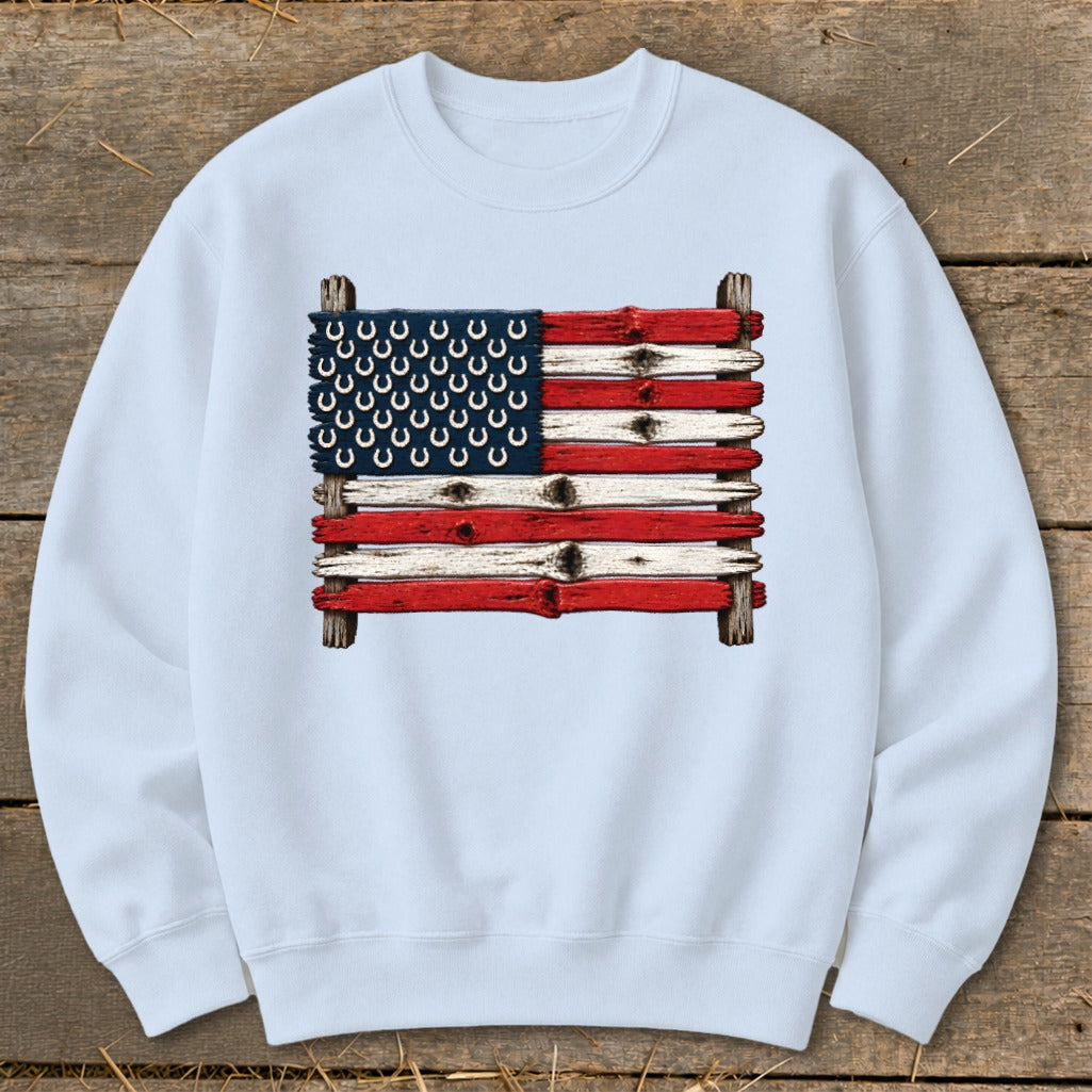 Light blue crewneck sweatshirt featuring a graphic of an American flag made from weathered wooden planks and horseshoes.