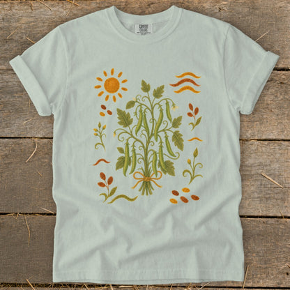 Light blue t-shirt with a botanical illustration of pea pods and a sun.