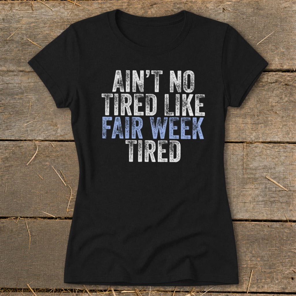 Black t-shirt with distressed white and blue text that says "AIN'T NO TIRED LIKE FAIR WEEK TIRED".