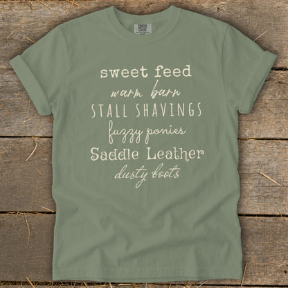 Sage t-shirt with white text: sweet feed, warm barn, stall shavings, fuzzy ponies, saddle leather, dusty boots.