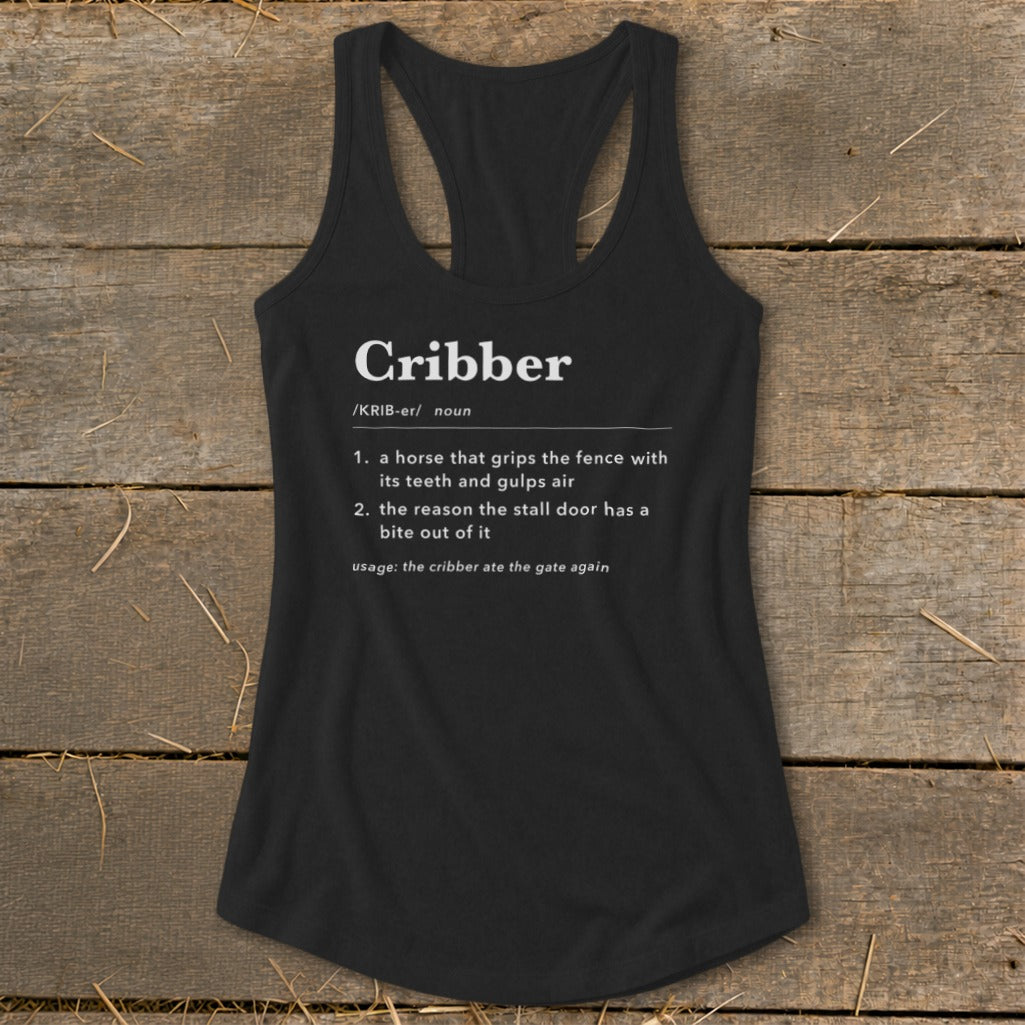 A black racerback tank top featuring white dictionary definition text for the word Cribber, laid flat on a rustic wooden surface.