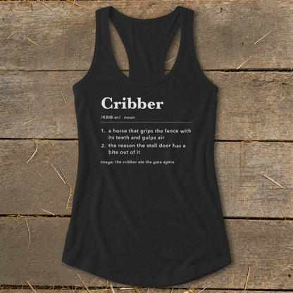 A black racerback tank top featuring white dictionary definition text for the word Cribber, laid flat on a rustic wooden surface.