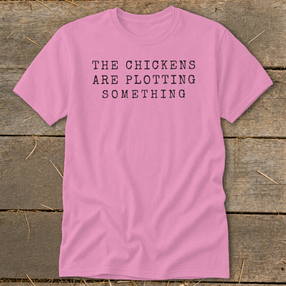 Pink t-shirt with black text that reads "THE CHICKENS ARE PLOTTING SOMETHING".