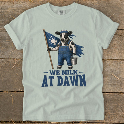 Cow in overalls with a flag and bucket, text reads "WE MILK AT DAWN".