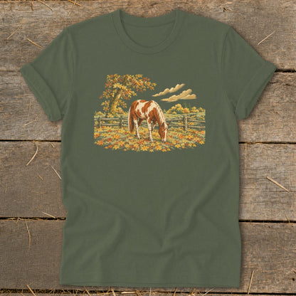 Brown and white horse grazing in a fall meadow with a wooden fence and autumn trees.