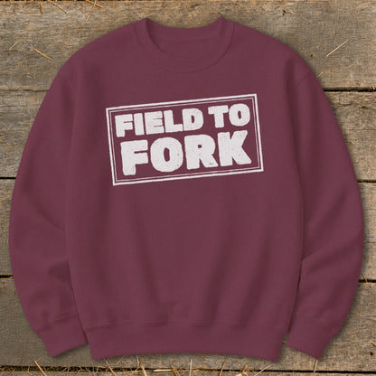 A maroon crewneck sweatshirt featuring a white rectangular stamp with the text FIELD TO FORK.