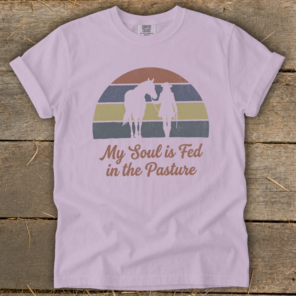 Light purple t-shirt with graphic of cowboy and horse under striped sunset, text "My Soul is Fed in the Pasture."