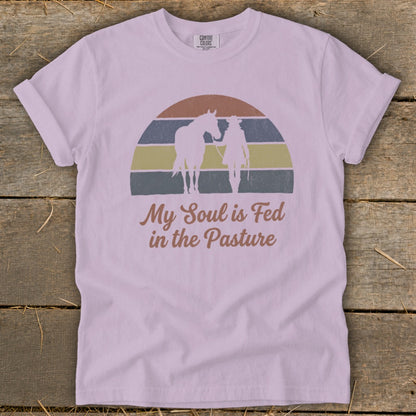 Light purple t-shirt with graphic of cowboy and horse under striped sunset, text "My Soul is Fed in the Pasture."