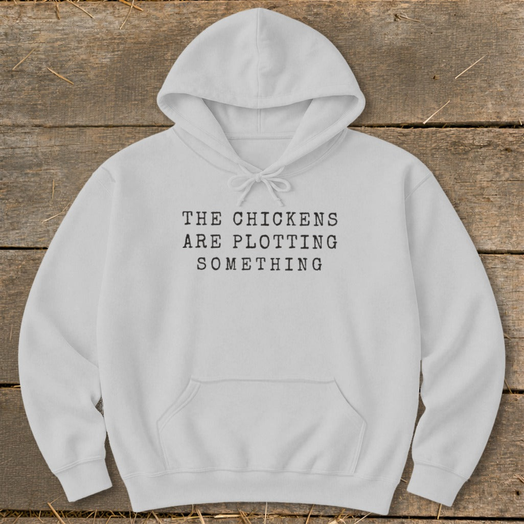 White hoodie with black text reading "THE CHICKENS ARE PLOTTING SOMETHING".