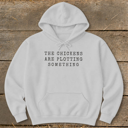 White hoodie with black text reading "THE CHICKENS ARE PLOTTING SOMETHING".