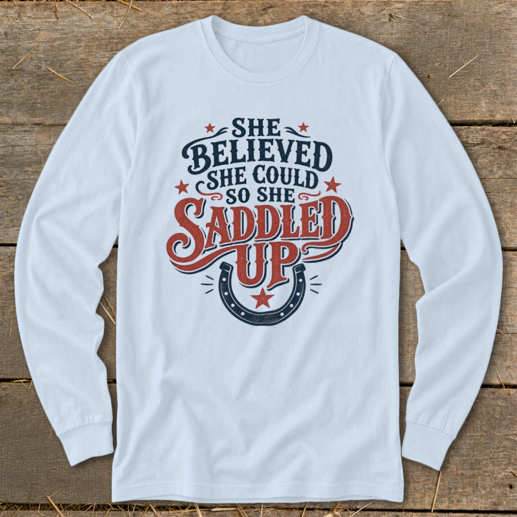 Long sleeve white shirt with "She Believed She Could So She Saddled Up" text and horseshoe graphic.
