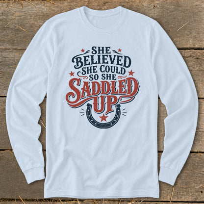 Long sleeve white shirt with "She Believed She Could So She Saddled Up" text and horseshoe graphic.