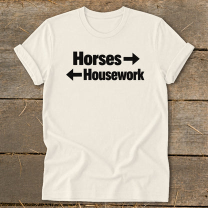 Cream-colored crewneck t-shirt with black text reading Horses and Housework, separated by directional arrows.