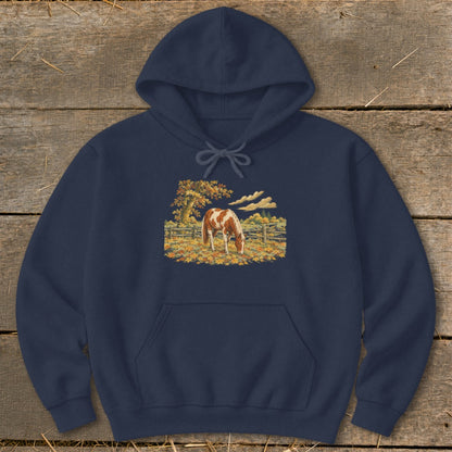 Navy hoodie with brown and white horse grazing in autumn leaves.