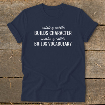 Navy t-shirt with white text reading "raising cattle BUILDS CHARACTER working cattle BUILDS VOCABULARY."