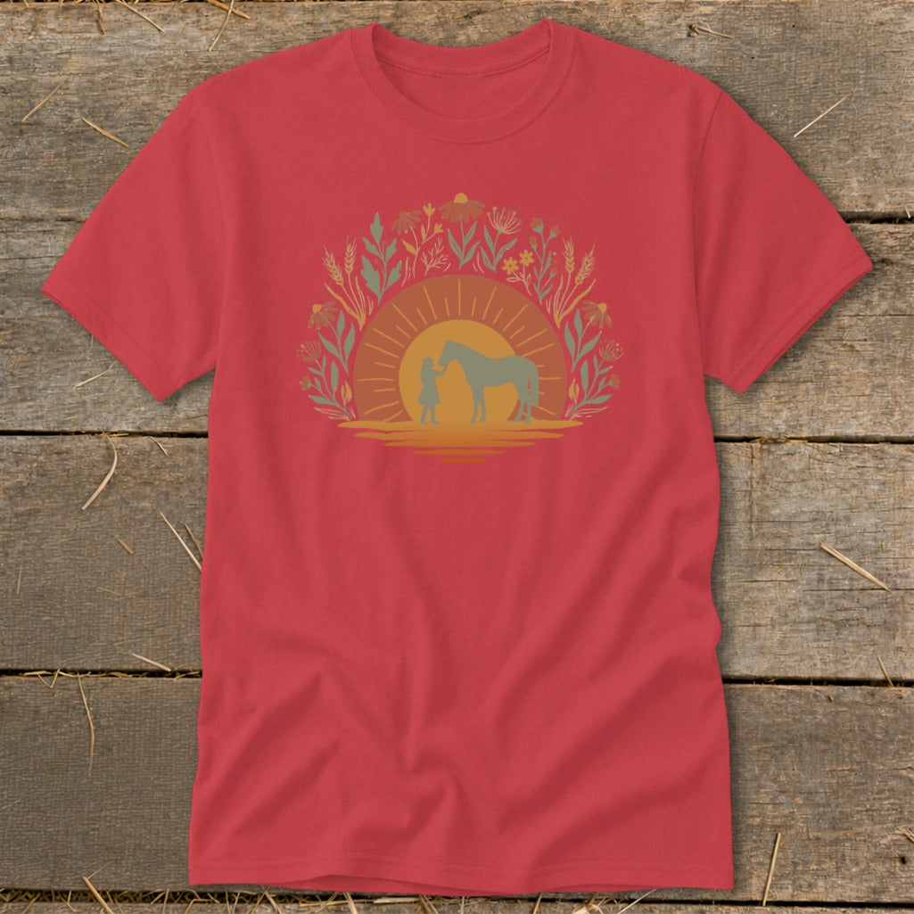 Red t-shirt with silhouette of child and horse against a sunset and floral border.