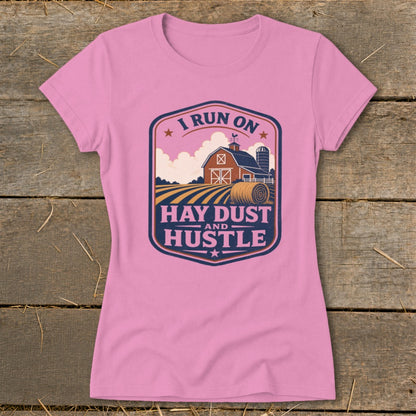 Pink t-shirt with farm graphic and text "I RUN ON HAY DUST AND HUSTLE".