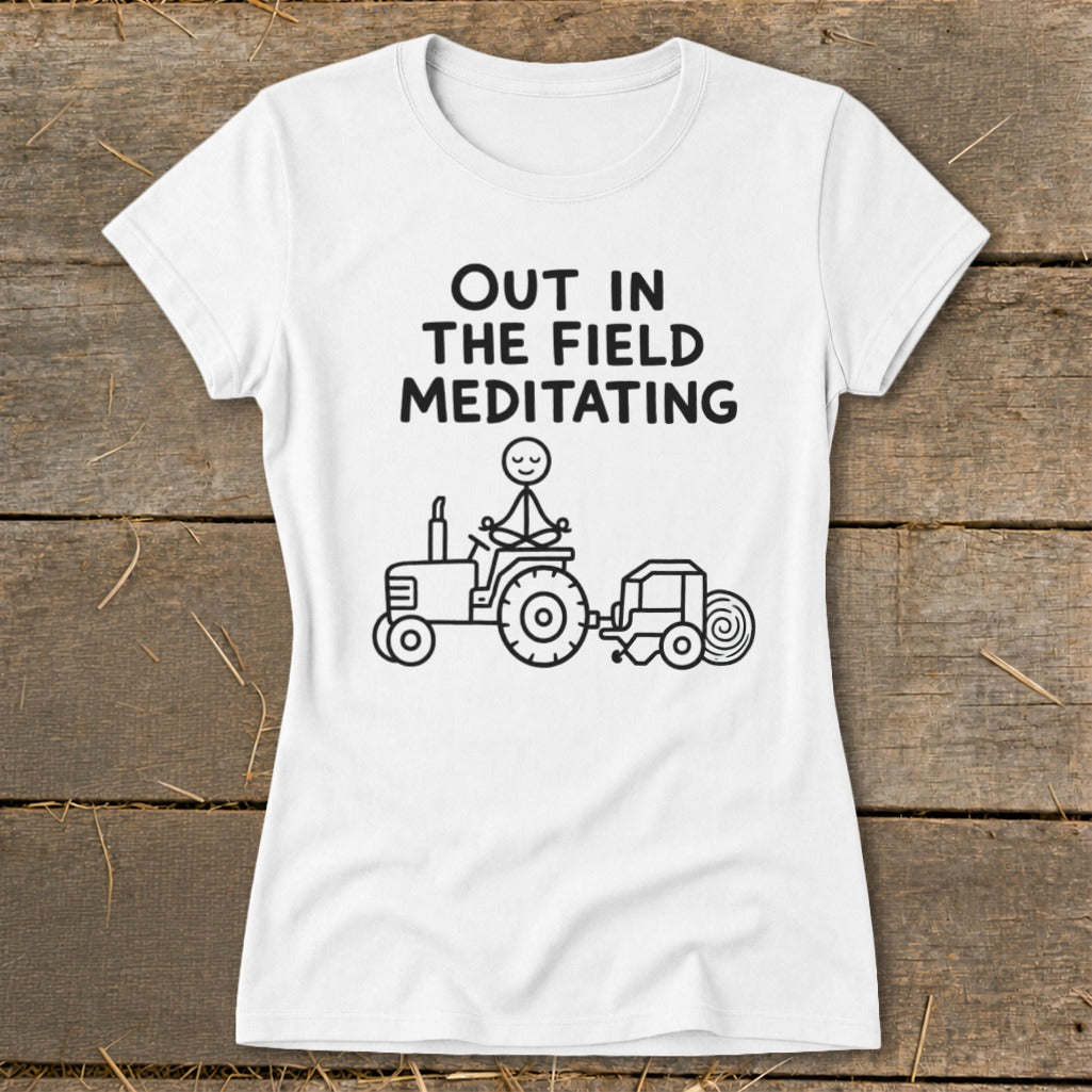 White t-shirt with graphic of person meditating on a tractor, text reads "OUT IN THE FIELD MEDITATING".
