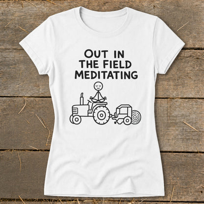 White t-shirt with graphic of person meditating on a tractor, text reads "OUT IN THE FIELD MEDITATING".