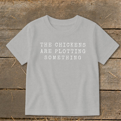 Light grey t-shirt with white text that reads "THE CHICKENS ARE PLOTTING SOMETHING".
