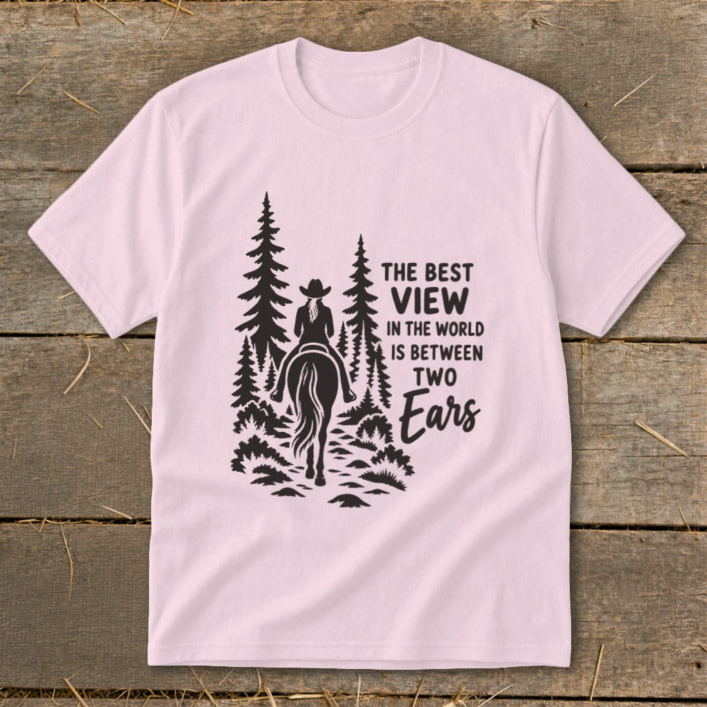 Light pink crewneck t-shirt featuring a black graphic of a horseback rider and pine trees with the text The Best View in the World is Between Two Ears.