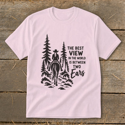 Light pink crewneck t-shirt featuring a black graphic of a horseback rider and pine trees with the text The Best View in the World is Between Two Ears.