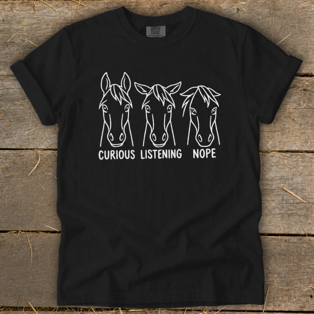 A black t-shirt displays a white graphic of three horse heads with the text "CURIOUS," "LISTENING," and "NOPE."
