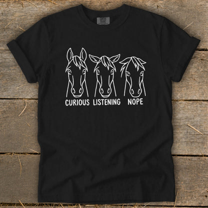 A black t-shirt displays a white graphic of three horse heads with the text "CURIOUS," "LISTENING," and "NOPE."