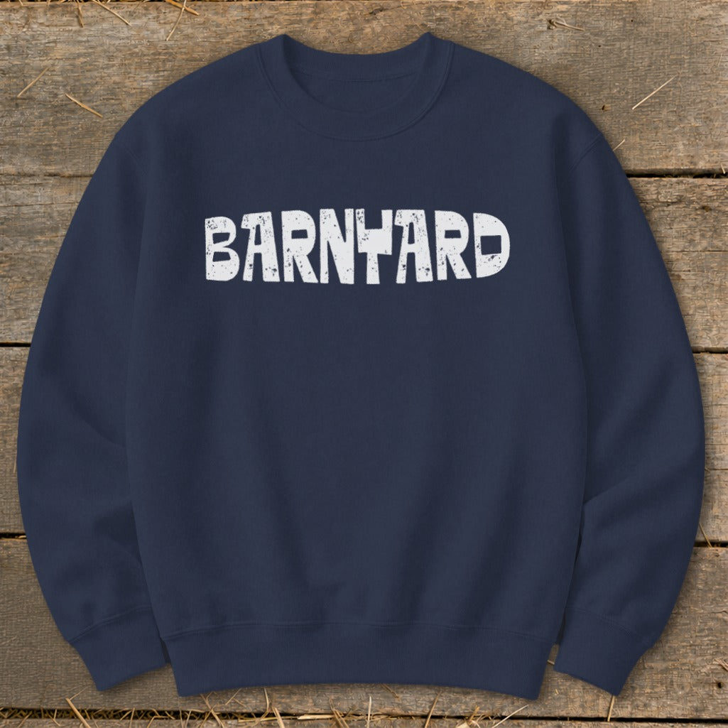 Dark blue crewneck sweatshirt with white distressed text reading BARNYARD centered on the chest, lying flat on a wooden background.