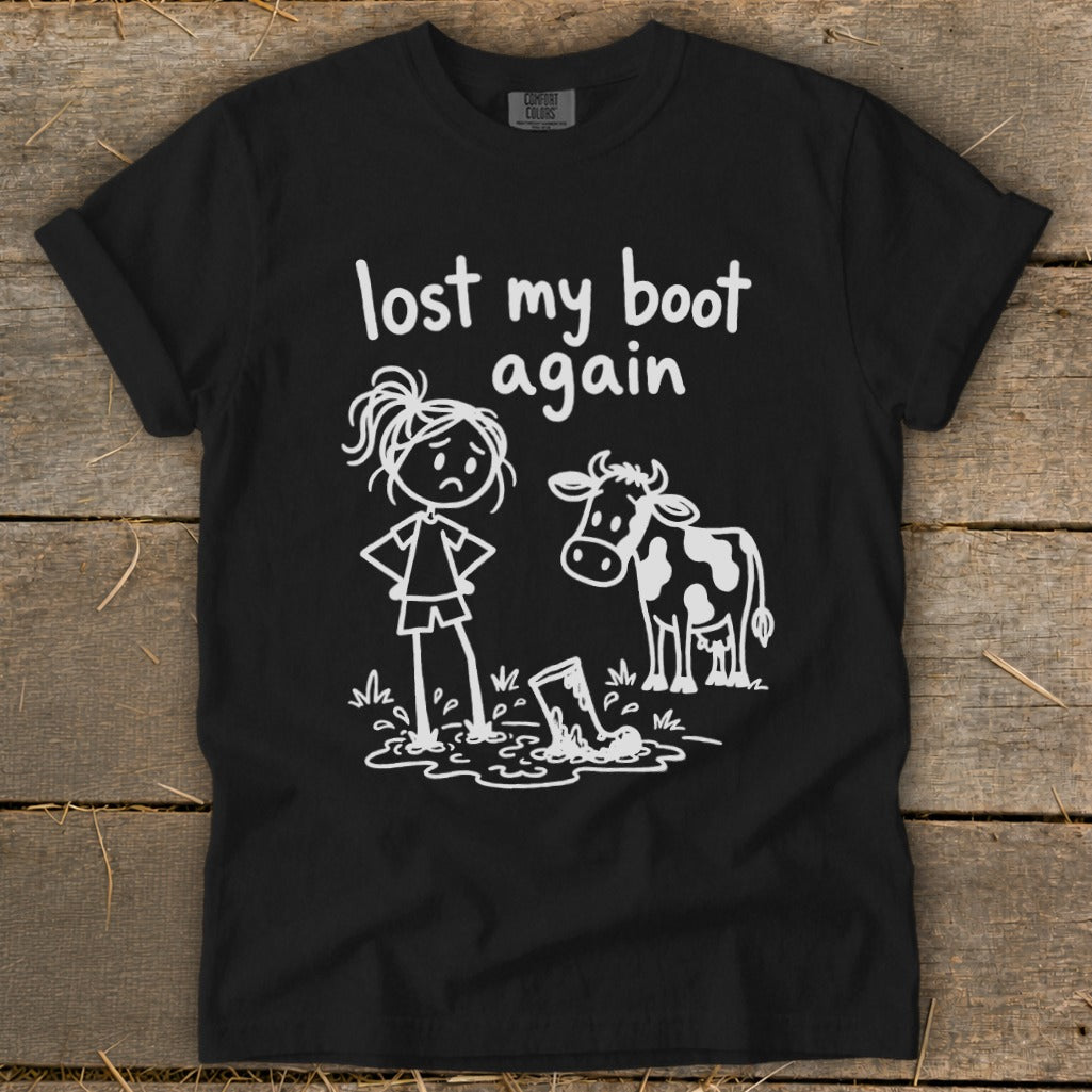 Black t-shirt featuring white line art of a sad person and a cow looking at a muddy boot next to text reading "lost my boot again."