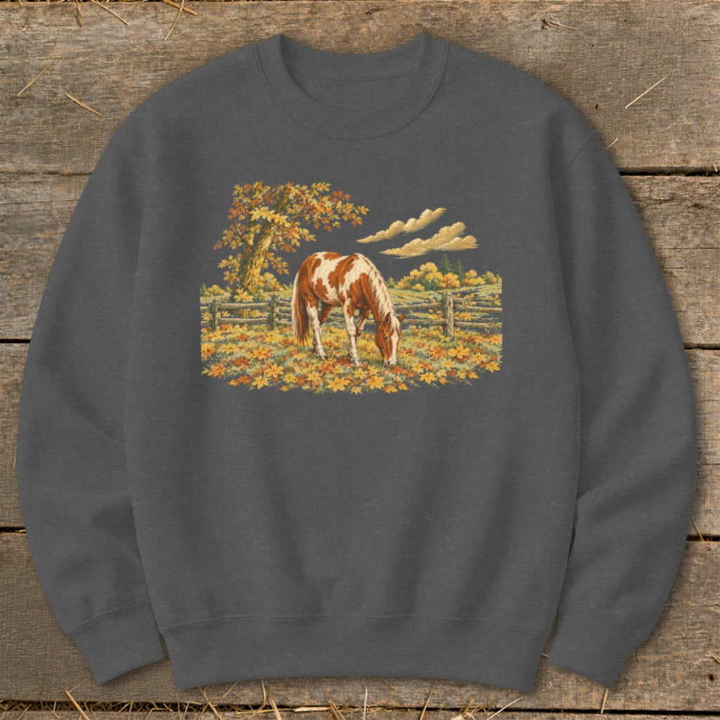 Brown and white horse grazing in a field of autumn leaves near a wooden fence.