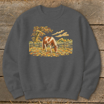 Brown and white horse grazing in a field of autumn leaves near a wooden fence.