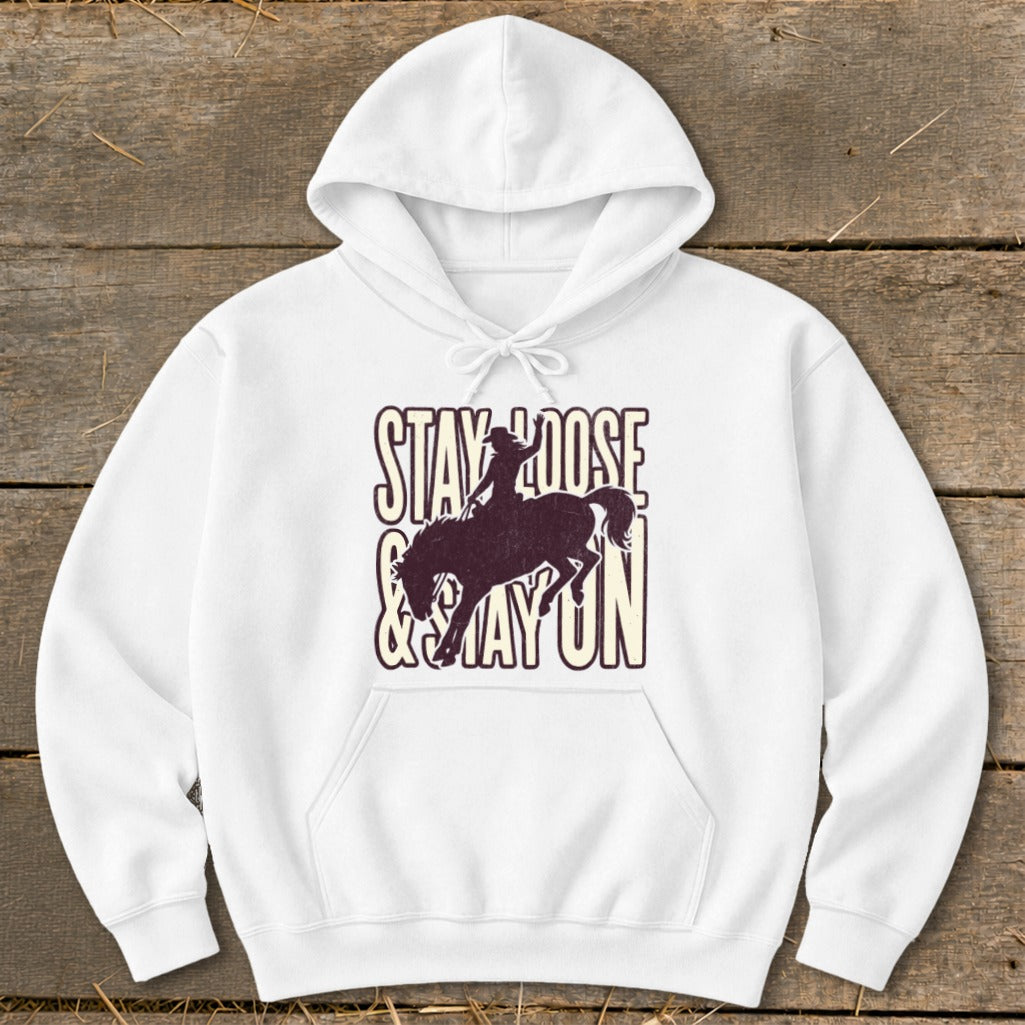 White hoodie with "STAY LOOSE & STAY ON" text and a silhouette of a rider on a bucking horse.