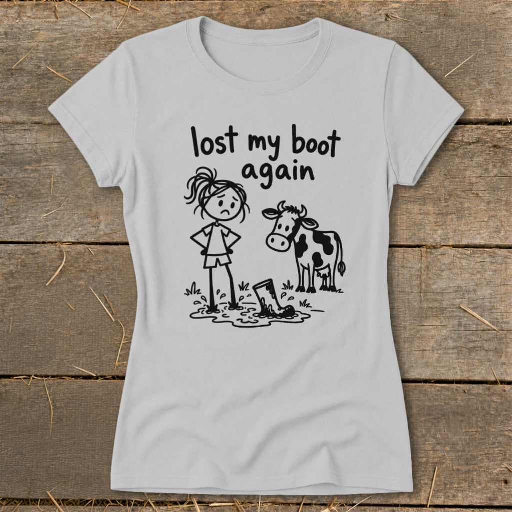 Light gray short-sleeved t-shirt with a graphic of a sad stick-figure girl and a cow looking at a muddy boot, with text reading "lost my boot again".