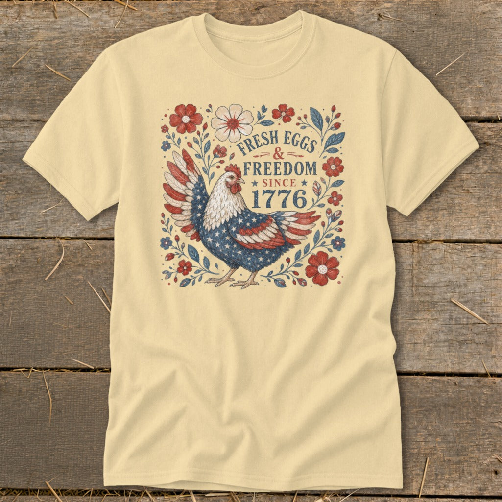 Light yellow t-shirt with patriotic chicken design and text "Fresh Eggs & Freedom Since 1776".
