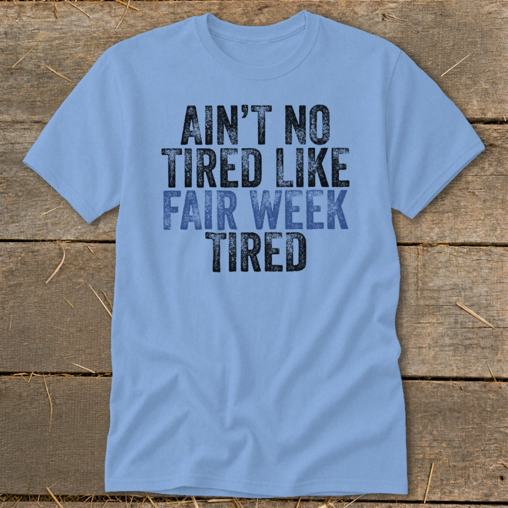 Light blue t-shirt with black and blue text that reads "Ain't No Tired Like Fair Week Tired".
