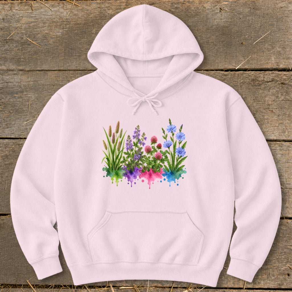 Light pink hooded sweatshirt featuring a colorful watercolor wildflower graphic on the chest, laid flat on wood.
