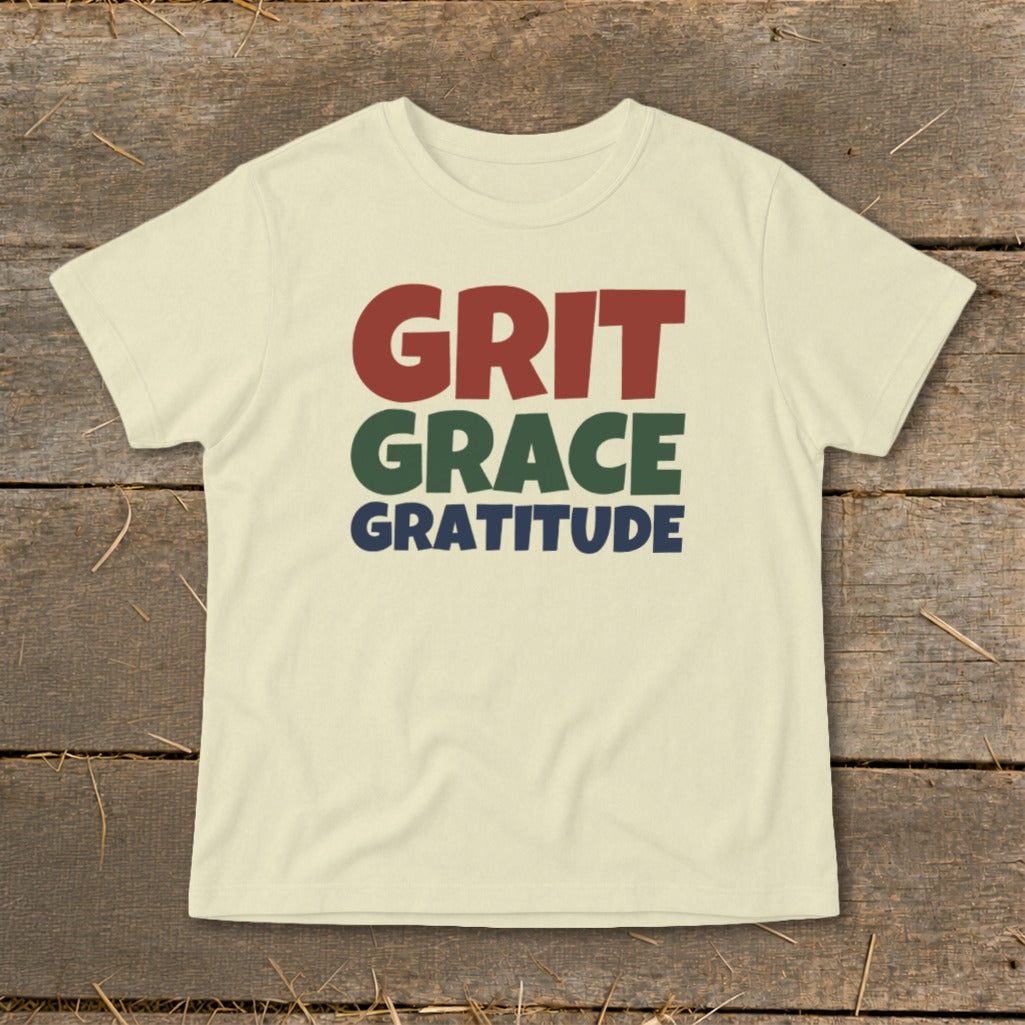 A cream-colored short-sleeved t-shirt with the words Grit, Grace, and Gratitude printed in red, green, and blue.