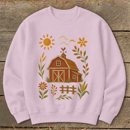 Pink sweatshirt with a red barn, sun, flowers, and fence graphic.