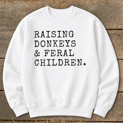 White sweatshirt with black text reading "RAISING DONKEYS & FERAL CHILDREN."