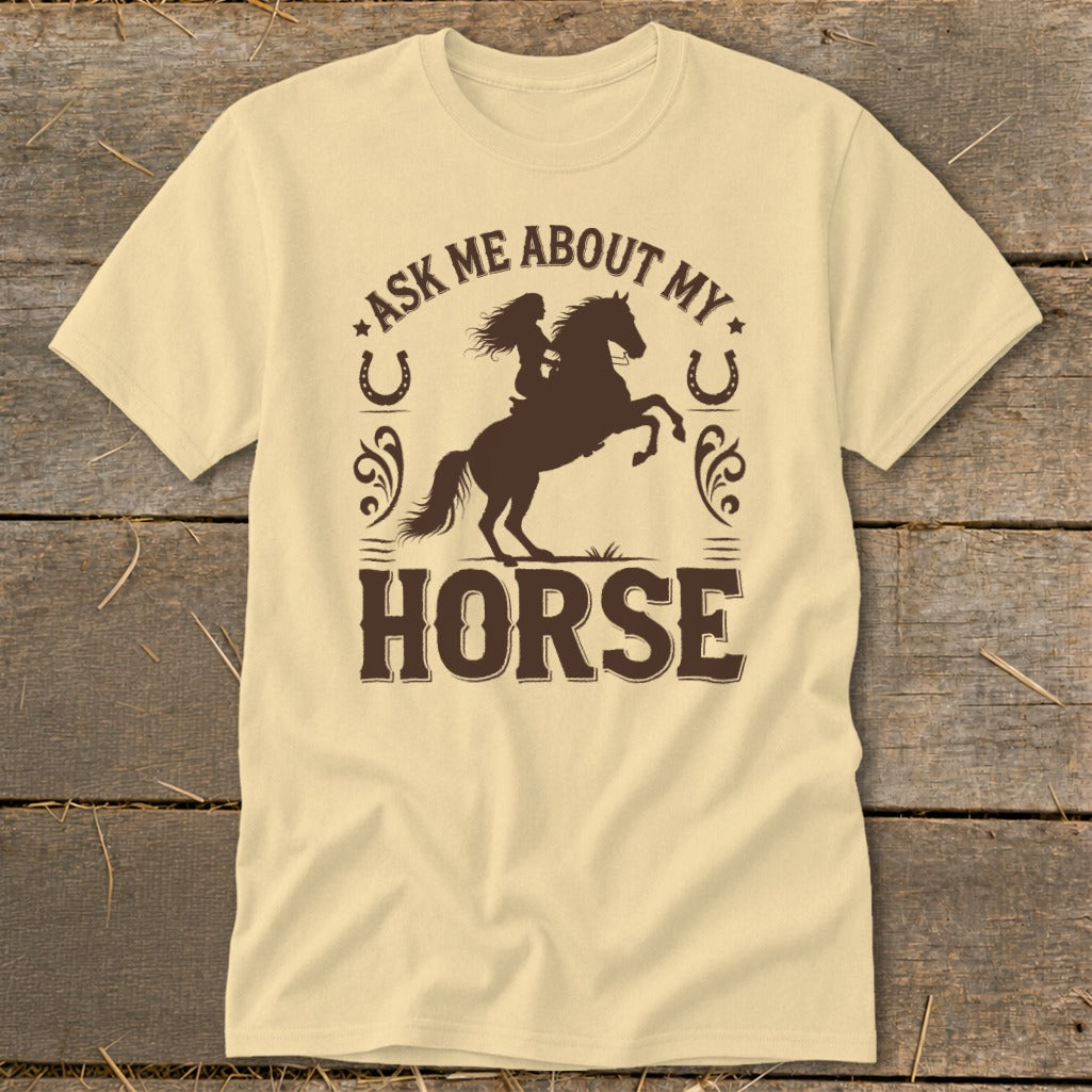 Light yellow t-shirt with brown graphic of a woman riding a bucking horse and text "ASK ME ABOUT MY HORSE".