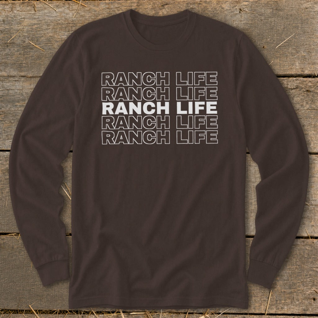 A brown long-sleeve t-shirt with the words RANCH LIFE repeated in stacked white outlined font on a rustic wooden background.