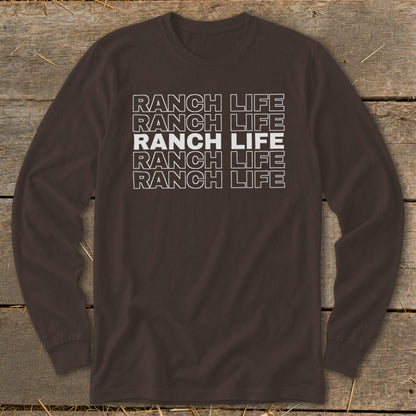 A brown long-sleeve t-shirt with the words RANCH LIFE repeated in stacked white outlined font on a rustic wooden background.